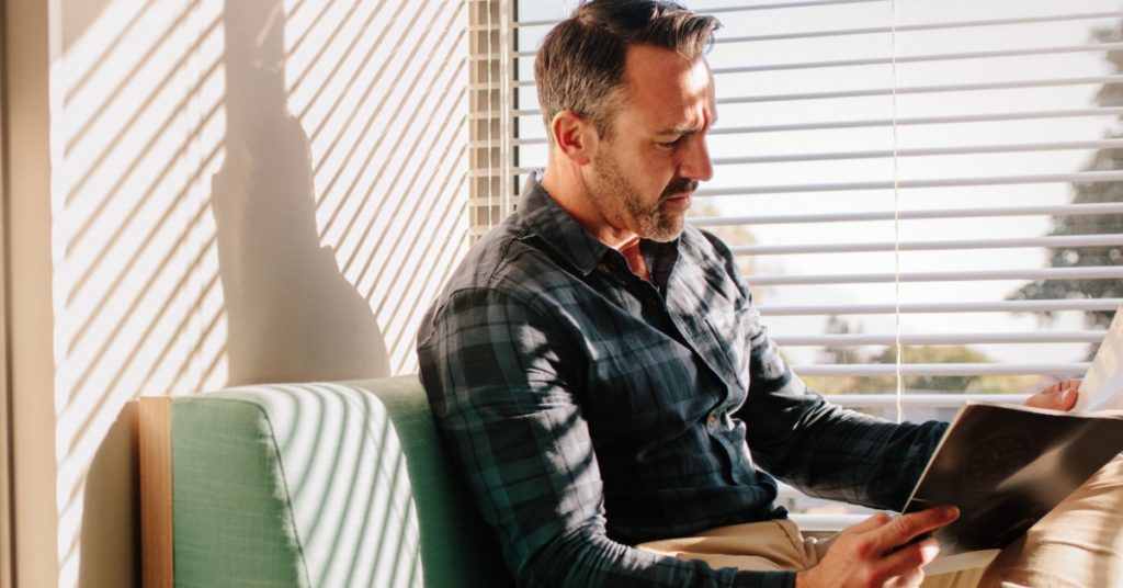 image of a middle aged man sitting in a waiting room reading a pamphlet