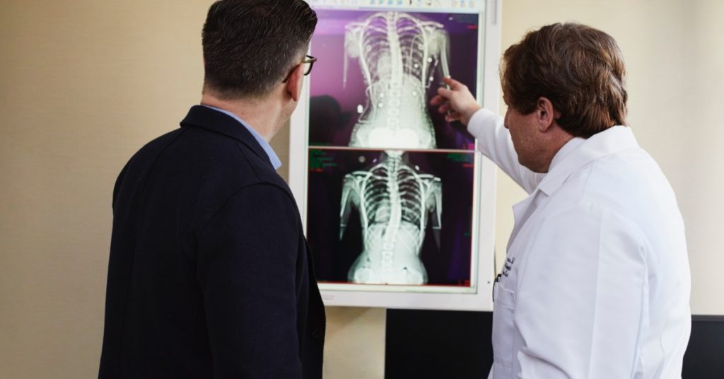 image of the back of two men, one in a blue blazer and one in a lab coat, looking at medical imaging prints