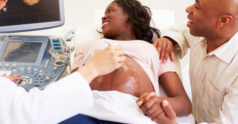 image of an African American woman having an ultrasound of her pregnant belly. a man is holding her hand and smiling at the ultrasound screen