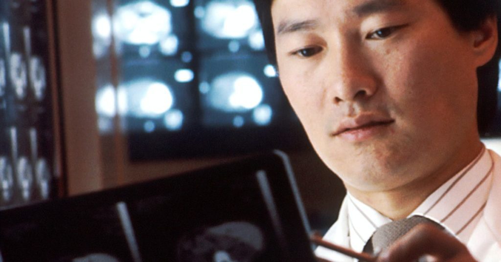 close up image of an Asian doctor's face reviewing a CT image