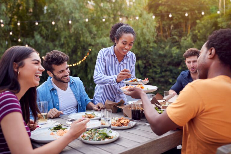 Friends At Home Sitting At Table Enjoying Food At Summer Garden Party